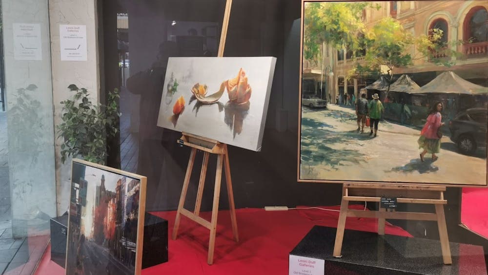 Paintings displayed in a gallery window, including realist still life and street scene artworks on e
