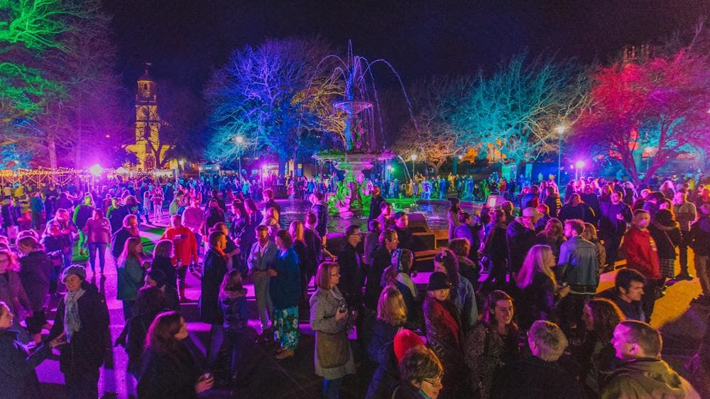A crowd of people lit up by multicoloured lights outside at night