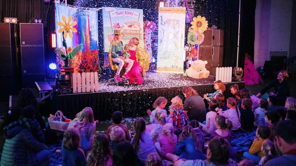 Colourful lit stage with children's performer and crowd of young children audience members