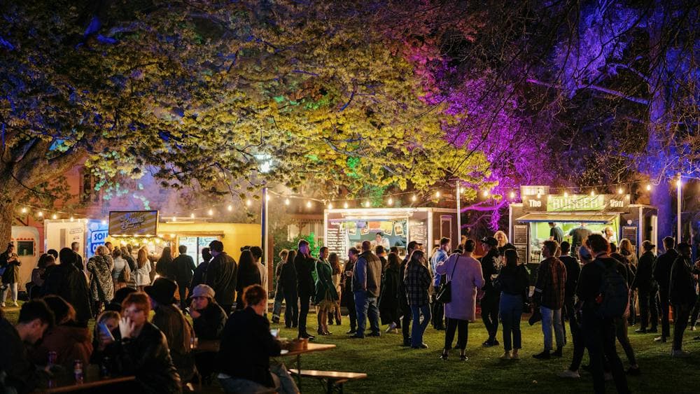 People mingle under colourful lights new food vans