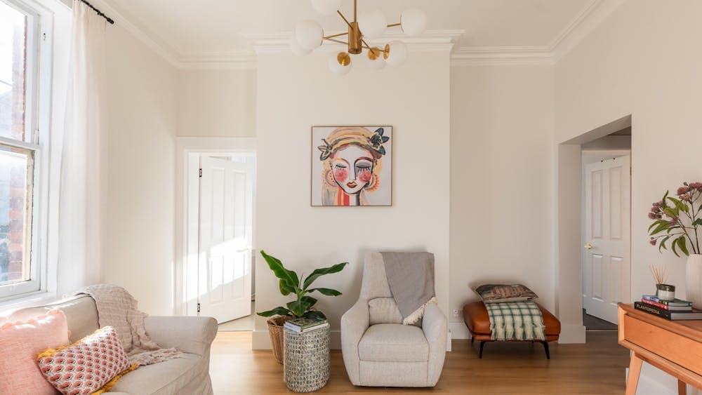 Living room with sofa, occasional chair, plant, chandelier, light curtains