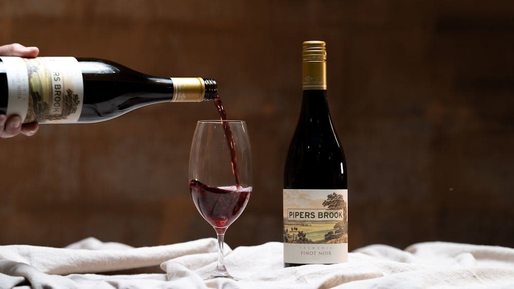 A bottle of Tasmanian Pinot Noir being poured into a glass in a warmly lit cellar.