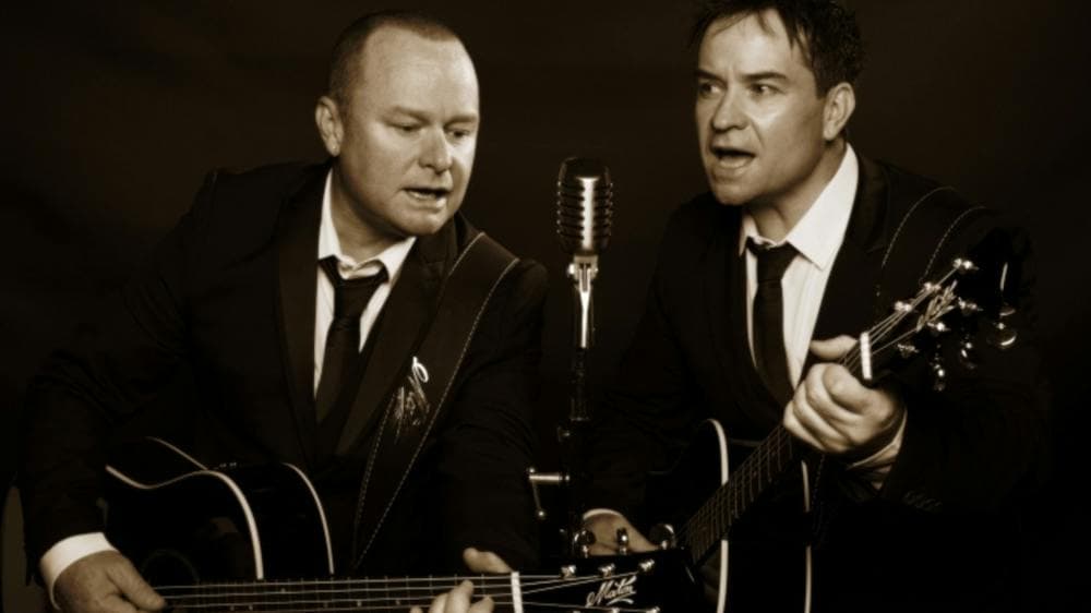 Two men playing guitars and singing into a microphone